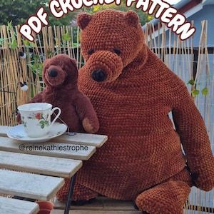 May include: A large brown crocheted bear and a smaller brown plush bear sitting together. A white teacup with a floral pattern and a saucer sit on a wooden table. The text PDF CROCHET PATTERN is visible at the top and @reinekathiestrophe at the bottom.