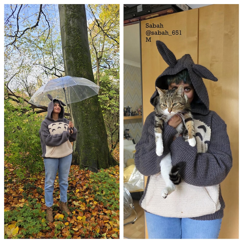 May include: A gray hooded sweatshirt with a Totoro design, featuring a cream-colored belly and a pocket. The hood has large, pointed ears. The person is wearing blue jeans and brown boots, holding a clear umbrella in a forest setting.