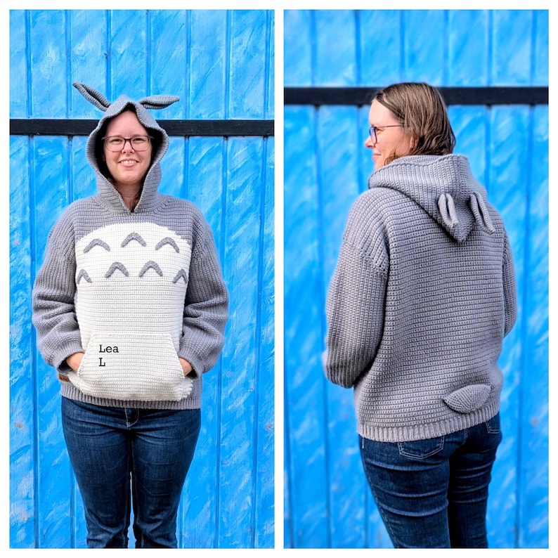 May include: A gray and white hooded sweatshirt with a cartoon design, featuring a kangaroo pocket and a hood with attached ears. The sweatshirt is worn with blue jeans. The text "Lea L" is visible on the front.