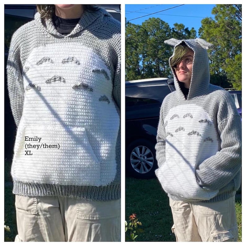 May include: A gray and white crochet hoodie with a character design. The hoodie features a large white front panel with a pocket and embroidered details. The hood has pointed ears. The text "Emily (they/them) XL" is visible.