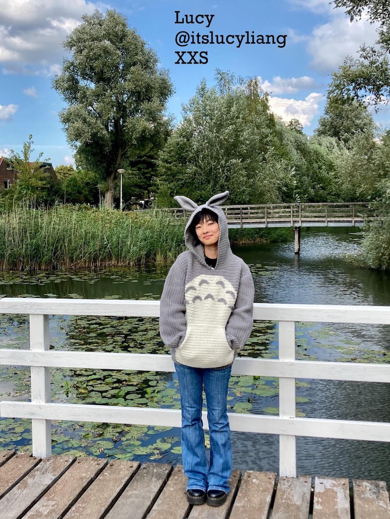 May include: A gray hooded sweatshirt with a Totoro design and attached bunny ears. The sweatshirt has a large cream-colored pocket and is worn with blue jeans. Text on the image reads "Lucy @itslucyliang XXS".