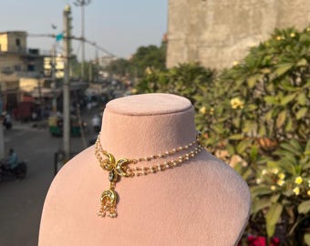 May include: A gold-toned necklace with a double strand of small, white beads. The necklace features crescent moon and teardrop-shaped pendants with intricate detailing and small, dangling beads. The necklace is displayed on a pink mannequin.