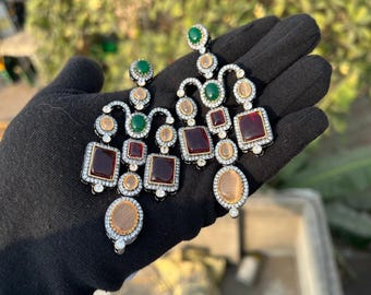 Può includere: Un paio di orecchini pendenti con finitura argentata. Gli orecchini presentano una cascata di pietre quadrate e ovali in tonalità di rosso, verde e beige.