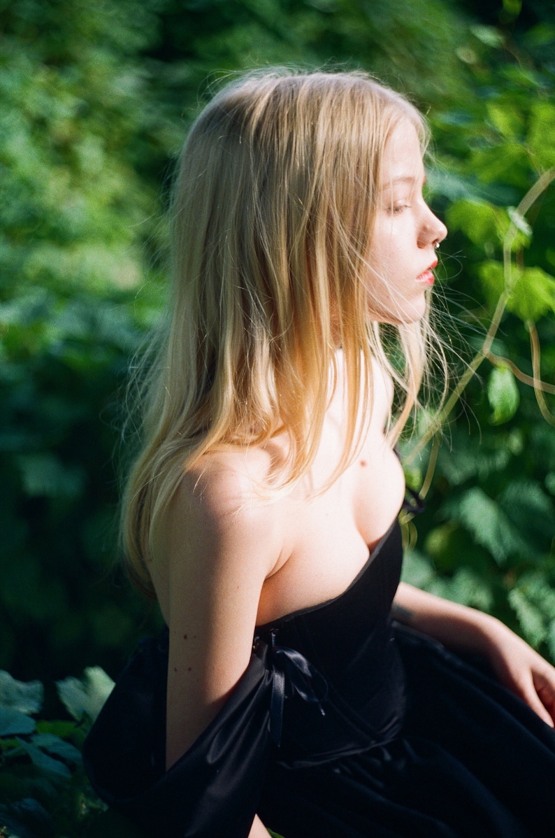 May include: A woman with long blonde hair wearing a black strapless dress with a sweetheart neckline. The dress has a black ribbon detail on the shoulder.