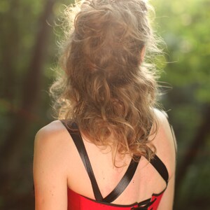 May include: A red corset with black straps and a lace-up back. The corset is worn by a person with long, curly hair.
