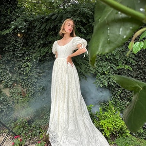 May include: A white lace wedding dress with a scoop neck, puff sleeves, and a long train. The dress is fitted at the bodice and flows out into a full skirt.
