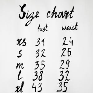 May include: A white size chart with black handwritten text. The chart lists sizes XS, S, M, L, and XL with corresponding bust and waist measurements in inches. The bust column shows 31, 32, 35, 38, 43 and the waist column shows 24, 26, 29, 32, 35.