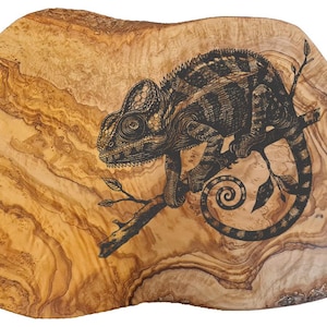 Könnte beinhalten: Ein Holz-Servierbrett mit natürlicher Holzmaserung. Das Brett ist mit einer detaillierten Schwarzweiß-Illustration eines Chamäleons auf einem Ast verziert.