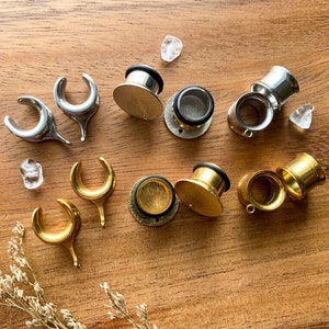 May include: Assortment of silver and gold ear gauges in various sizes and styles. The gauges are made of metal and have a smooth finish.
