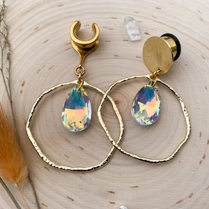 May include: A pair of gold hoop earrings with a teardrop-shaped iridescent crystal hanging from each hoop. The earrings are made of metal and have a textured finish.