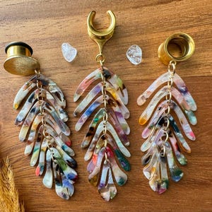 May include: Three pairs of gold and multi-colored acrylic dangle earrings with a leaf design. The earrings are attached to a gold metal hoop.