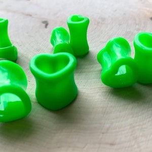 May include: A set of six green heart-shaped ear gauges. The gauges are made of a smooth, shiny material and are available in a variety of sizes.