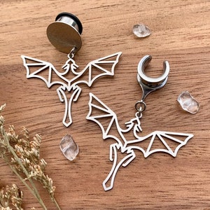 May include: Two silver dragon earrings with a dangling design. The earrings are made of metal and have a detailed dragon design. The earrings are perfect for adding a touch of whimsy to any outfit.