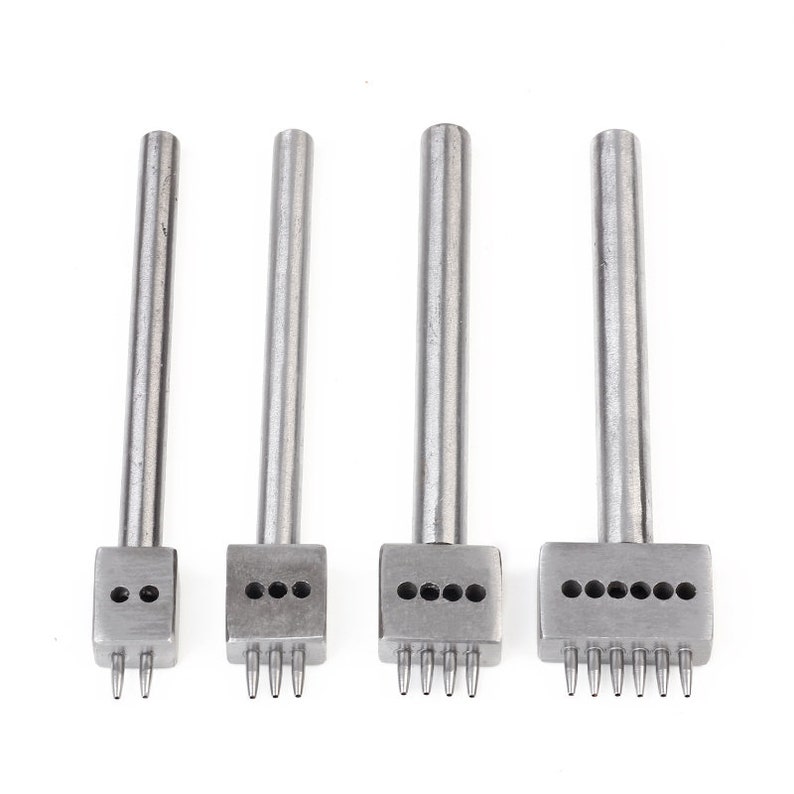 May include: Four silver leather hole punches with different numbers of holes. The punches are arranged from left to right with increasing numbers of holes. The punches are all the same length and have a similar design.