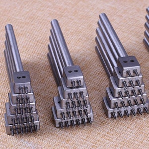 May include: Set of six silver leather hole punch tools with multiple punch sizes. Each tool has a stack of punch heads with different numbers of holes.