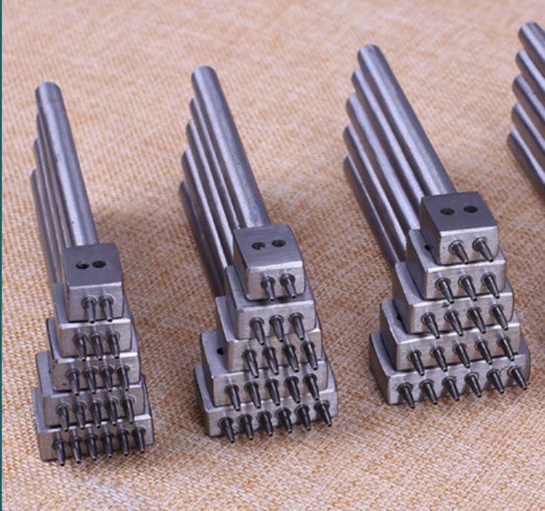 May include: Set of six silver leather hole punch tools with multiple punch sizes. Each tool has a stack of punch heads with different numbers of holes.