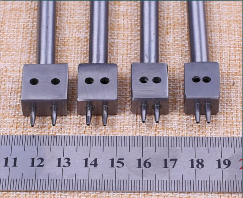 May include: Four silver leather hole punch tools with three prongs each. The tools are lined up in a row and are numbered 11 through 19 on a ruler.