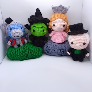May include: Four crocheted stuffed toys: a green witch, a pink princess, a gray and blue unicorn, and a black and green man with a top hat. The toys are sitting on balls of yarn.