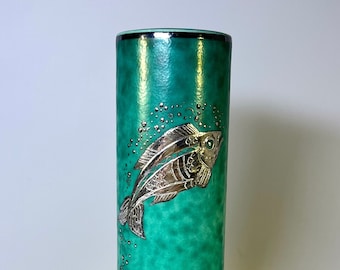 May include: A tall, cylindrical vase with a green glaze and a silver fish design. The vase has a flared base and a black rim.