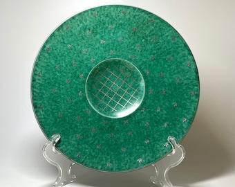 May include: A large, round, green ceramic serving plate with a smaller, raised, circular section in the center. The center section has a grid pattern and the plate is decorated with a repeating pattern of small, silver dots.