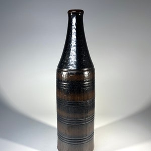 May include: A black and brown ceramic vase with a textured surface and a narrow neck.