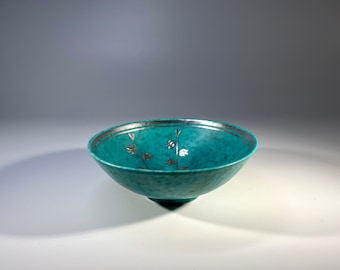 May include: A teal ceramic bowl with a silver floral design. The bowl has a slightly flared rim and a rounded base.