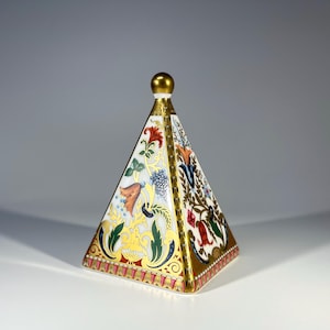 Puede incluir: Una tapa de porcelana blanca en forma de pirámide con un borde dorado y diseños florales en tonos rojos, naranjas, azules, verdes y amarillos.