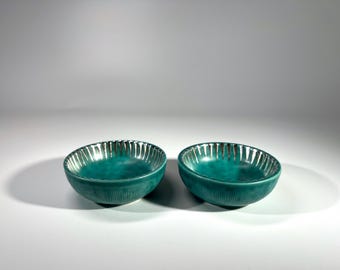 May include: Two teal green ceramic bowls with a silver rim and a textured surface.