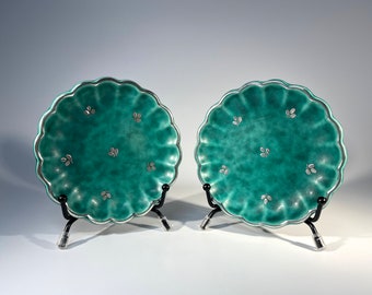 May include: Two teal ceramic plates with scalloped edges and silver leaf designs on black stands.