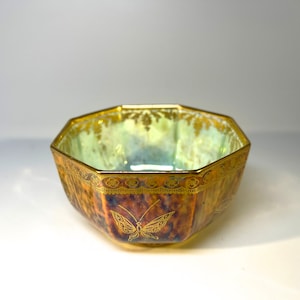 May include: Octagonal ceramic bowl with a gold rim and a butterfly design. The bowl has a brown and gold glaze with a iridescent finish.