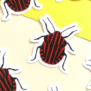 May include: A collection of red and black striped bug stickers on a yellow and beige background.