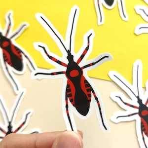 May include: A selection of insect stickers. Each sticker depicts a stylized insect with a black body, red markings, and white outlines. The stickers are displayed on a yellow and cream background.