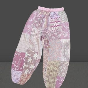 Może przedstawiać: Różowe spodnie w stylu patchwork z kwiatowym i geometrycznym wzorem. Spodnie mają sznurek w pasie i luźny krój.