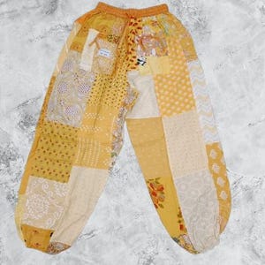 May include: Yellow patchwork trousers with a drawstring waist. The trousers are made of different fabrics and patterns, including floral, paisley, and geometric designs.
