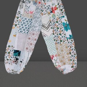 Peut inclure: Pantalon blanc avec un motif patchwork composé de différents motifs floraux dans des tons de bleu, vert, rose et jaune.
