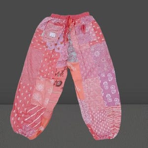 Puede incluir: Pantalones de color rosa con estampado de patchwork y cintura con cordón. Los pantalones están hechos de diferentes telas con estampados florales y geométricos.