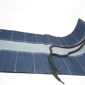 May include: A blue denim tool roll with multiple pockets and a black drawstring closure. The roll is unrolled and has a white label with the text "Royal Designs" and "Komelon" on it.