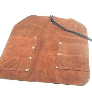 May include: A brown leather tool roll with multiple pockets and a drawstring closure. The roll has silver metal rivets and is designed to hold tools.