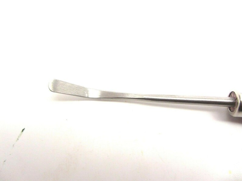 Puede incluir: Un primer plano de una herramienta de metal plateado con una cuchilla curva. La herramienta se utiliza para raspar y limpiar.