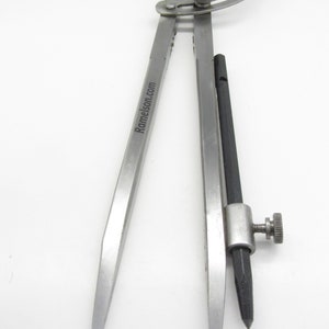 May include: A silver compass with a black adjustable point and a silver adjustment knob. The compass is engraved with the text "Ramelson.com".