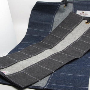 May include: A black and gray denim tool roll with white stitching and a gray and white denim lining. The roll has a label that says "Made by the Stitch".