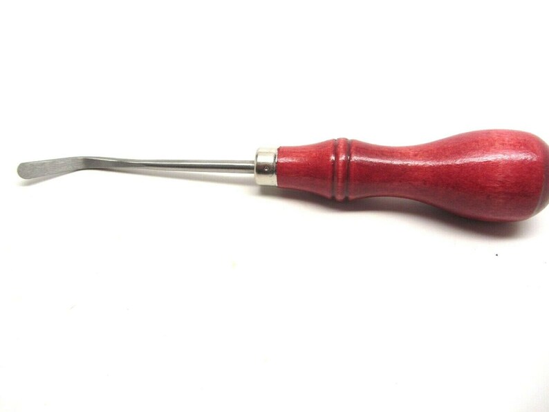 Puede incluir: Una herramienta de raspado de metal curvada con un mango de madera rojo. La herramienta se utiliza para raspar y limpiar.