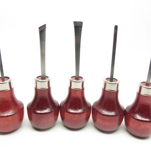 May include: Set of six wood carving tools with red wooden handles and silver metal ferrules. The tools have different shaped blades.