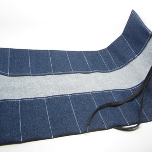 May include: A blue denim tool roll with a black drawstring closure. The roll has multiple pockets for storing tools.