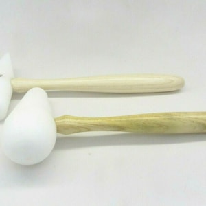 May include: Two wooden mallets with white striking heads. One mallet has a rounded head, the other has a flat head. The handles are made of light-colored wood. The mallets are likely used for woodworking or crafts.