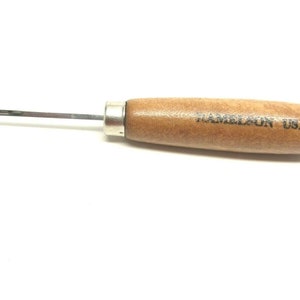 May include: A HAMELSON USA wood-handled tool with a metal shaft and tip. The handle is a light brown color, and the text "HAMELSON USA" is printed on the handle. The tool has a silver metal ferrule where the shaft meets the handle.