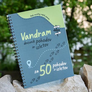 Puede incluir: Un cuaderno de espiral con una cubierta azul y verde claro que presenta el texto "Vandram dnevnik pohodov in izletov" y "za 50 pohodov ali izletov," junto con un gráfico de un camino discontinuo, huellas, un pin de ubicación y señales.