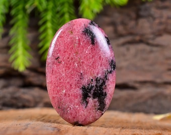 May include: A pink and black gemstone with a smooth, oval shape. The stone has a mottled pattern of pink and black.