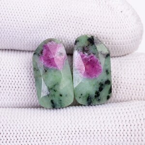 May include: Two green and pink gemstone cabochons with a faceted cut. The stones have a green base with pink and black inclusions.