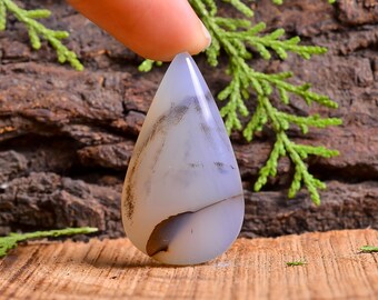 May include: A teardrop-shaped pendant made of white agate with brown and black inclusions. The pendant is smooth and polished.